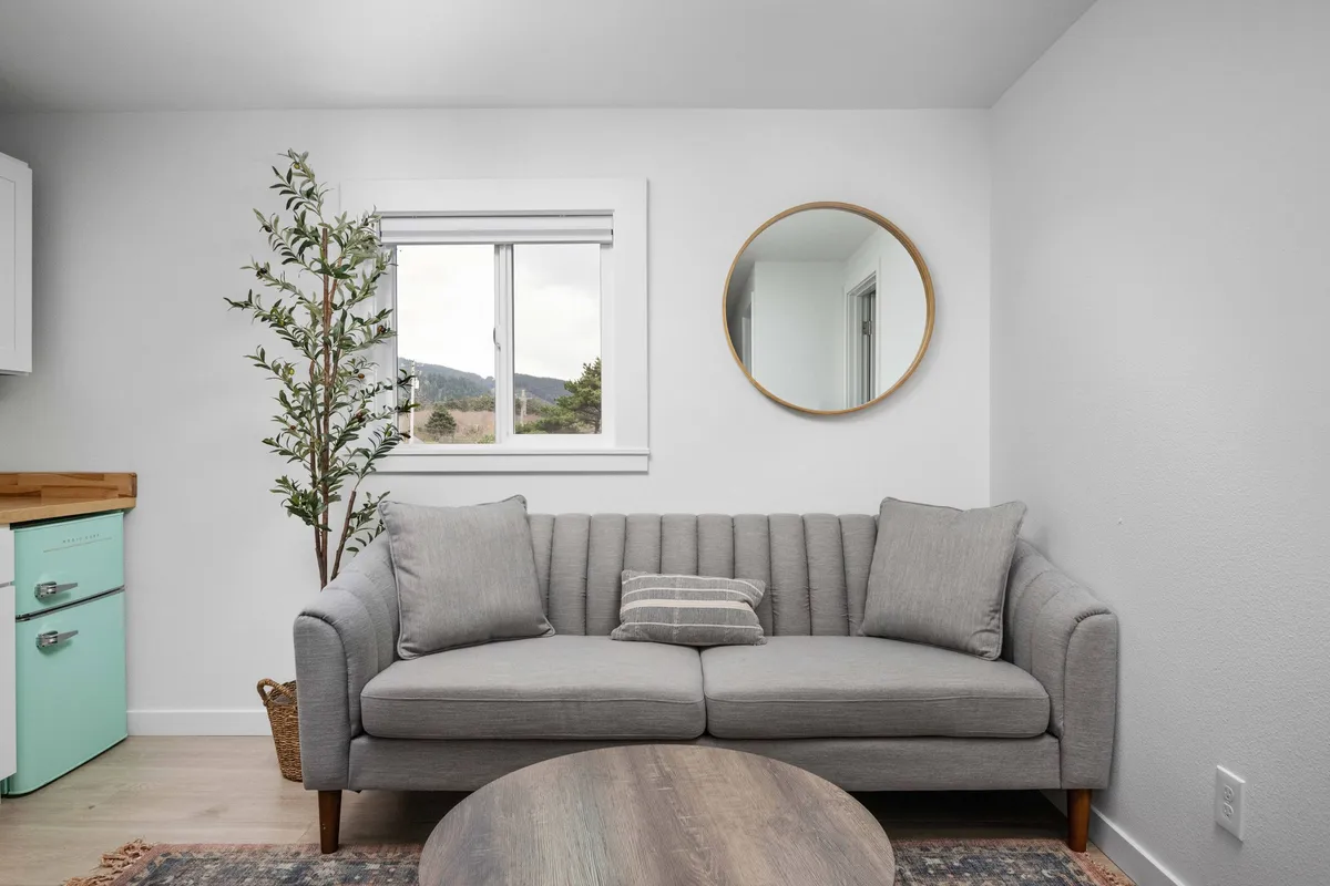 A cozy living area with a comfortable sofa, coffee table, lush green plant, and decorative mirror. The arrangement is perfect for relaxing, reading, or socializing after a day out, and it exudes a warm, homey vibe.
