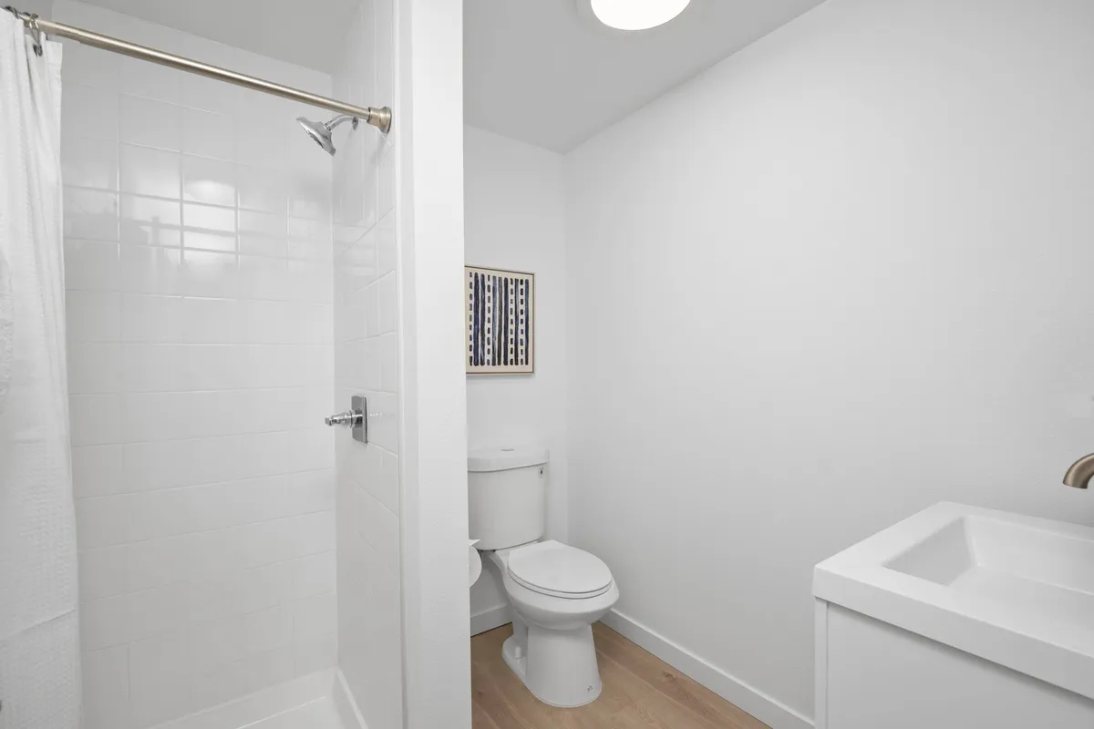 A bright, minimalistic bathroom interior with a walk-in shower, toilet, modern sink, and decorative wall art. The design feels fresh and recently remodeled, providing a clean and inviting space for guests to refresh and unwind.