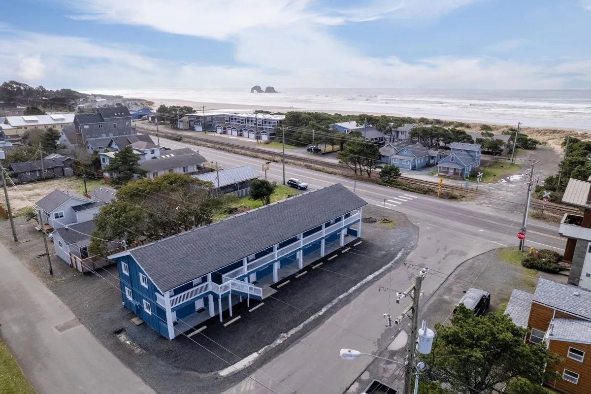 An exterior view of a blue building near the ocean, surrounded by other homes, with the beach and distant rock formations visible. The setting conveys immediate access to outdoor adventures, perfect for pet walks and exploration.